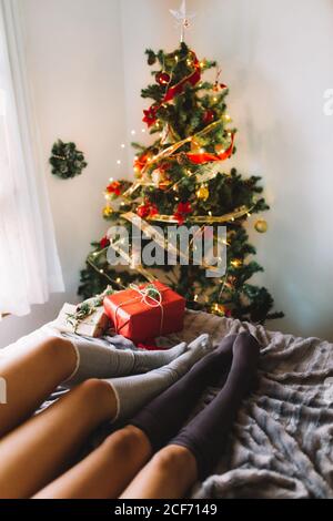 Two women friends with knee high socks in winter holidays at home near christmas tree and presents in cozy interior.