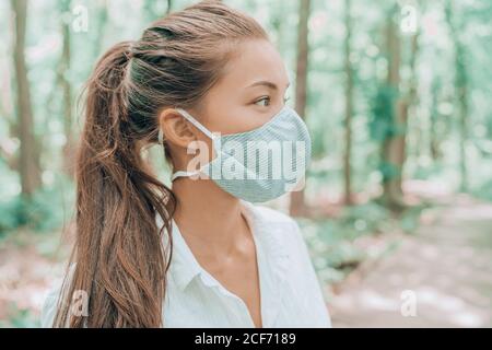 Face mask of cotton fabric are breathable for skin. Asian woman wearing corona virus mouth covering walking outdoors in woods Stock Photo