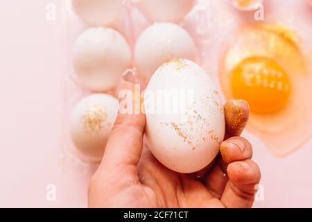 From above unrecognizable person holding festive glittered Easter egg during preparation for holidays on pink background Stock Photo
