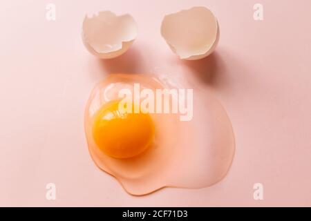 From above raw broken egg with yellow yolk and eggshells on pink background Stock Photo