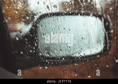 Wing mirror of modern car behind door window covered with water drops on rainy day Stock Photo