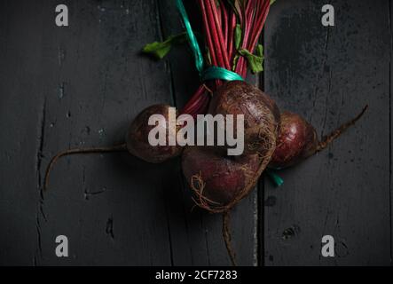 From above dark red sugar beetroots on stem with green leaves on black background Stock Photo