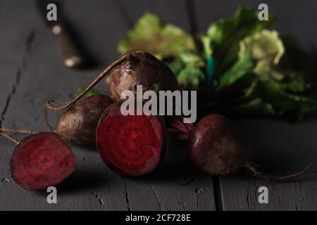 From above dark red sugar beetroots on stem with green leaves on black background Stock Photo