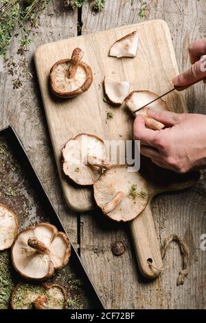 From above crop cook cutting caps of fresh brown Shiitake mushrooms on wooden cutting board at shabby rustic table Stock Photo