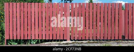There is an poor garden  and a village house behind a red  wooden  fence. Panoramic summer landscape from several outdoor photos Stock Photo
