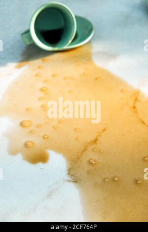 Hot aromatic brown beverage spilling from dropped cup on saucer to table Stock Photo