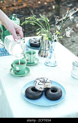 Woman pouring fresh milk from jug to ceramic mug while having picnic in garden Stock Photo