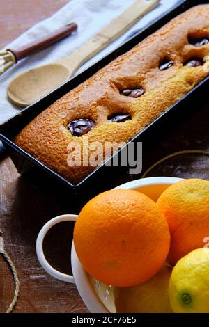 From above freshly baked sponge chocolate cake and ripe oranges placed on table near whisk and thread in kitchen Stock Photo