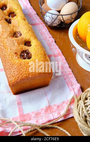 From above freshly baked sponge chocolate cake and ripe oranges placed on table near whisk and thread in kitchen Stock Photo