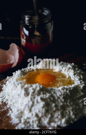 Broken egg in flour on textured black surface with round knife for cutting dough and glass pot Stock Photo