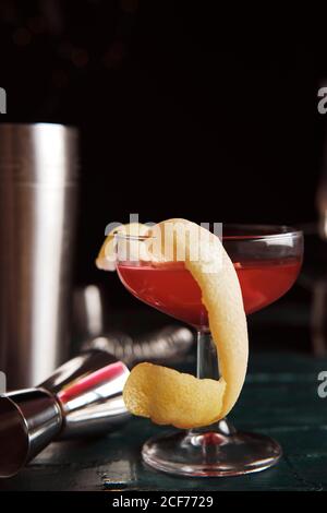 Front view set of coupe glasses with red alcohol cocktail garnished with green olive and lemon peel served on counter in bar Stock Photo