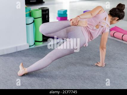 back view of flexible sportive concentrated brunette in sportswear doing lying yoga pose on mat Stock Photo