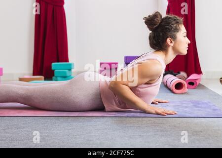 Side view of flexible sportive concentrated brunette in sportswear doing lying yoga pose on mat Stock Photo