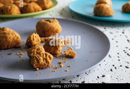 Fresh brown bitten cookies with chocolate crumbs lying on colorful ceramic plates on white spotted table against blurred white wall Stock Photo