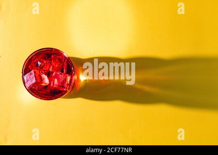 From above glass with tasty red drink and ice cubes on bright yellow surface in light Stock Photo