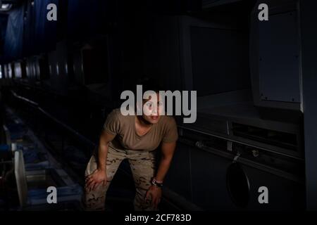 Side view of strong female soldier pointing up while looking at sky through ceiling window of military base Stock Photo