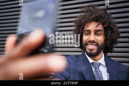 Bearded African American man with curly hair smiling while taking selfie next to striped wall Stock Photo