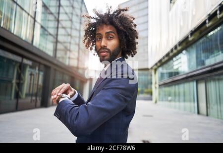 Joyful ethnic worker standing outside and checking time Stock Photo