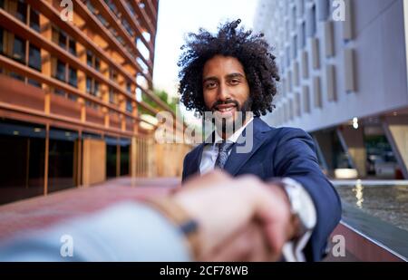 Ethnic happy businessman shaking hands with partner and looking at camera Stock Photo