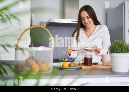Attractive young happy Woman making sandwiches at table in kitchen at home Stock Photo