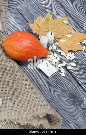 Orange pumpkin, seeds and candle stubs. Nearby are boxes of matches and dried maple leaves. On brushed pine boards painted black and white. Stock Photo