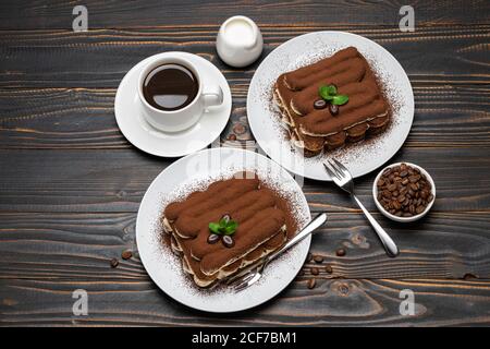Two portions of Classic tiramisu dessert, cup of coffee and milk or cream on wooden background Stock Photo