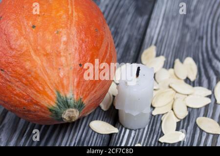 Orange pumpkin, seeds and candle stub. On brushed pine boards painted black and white. Stock Photo