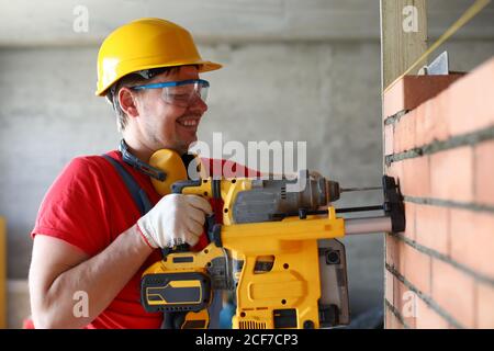 Builder drilling hole in wall, construction site Stock Photo