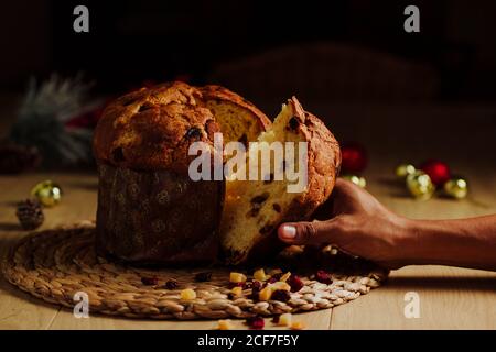 Panettone on a black background and man hand taking a slice. Stock Photo