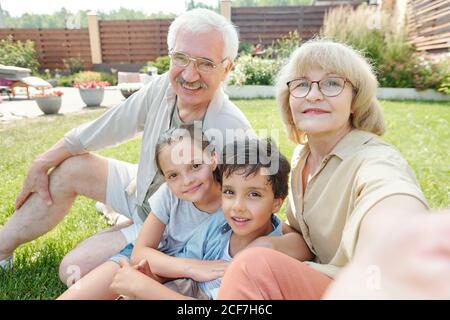 Modern grandma taking selfie shot of herself, her husband and grandchildren on smartphone camera Stock Photo