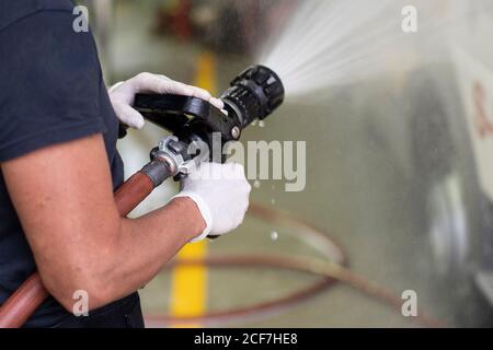 Side view of unrecognizable firefighter in latex gloves washing car with fire hose at station Stock Photo