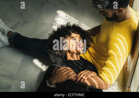 Pretty cheerful African American Woman smiling while lying on knees of bearded man in stylish room Stock Photo