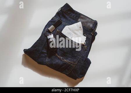 From above of folded jeans with white protective mask in pocket and car keys placed on white background in light studio Stock Photo