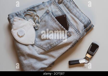 From above of folded jeans with white protective mask in pocket and car keys placed on white background in light studio Stock Photo