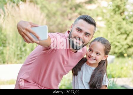 Modern young adult father wearing pale pink T-shirt taking selfie shot with his daughter, horizontal medium shot Stock Photo