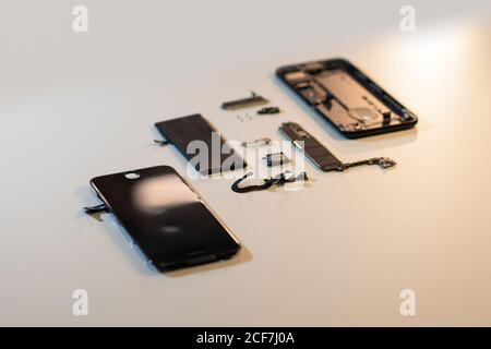 Details of damaged and disassembled mobile phone placed on white surface of repair workshop table Stock Photo