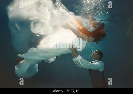 Side view of couple swimming together underwater in swimming pool after wedding ceremony Stock Photo