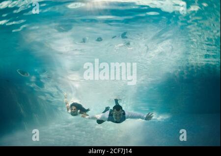 Happy couple swimming together underwater in swimming pool after wedding ceremony Stock Photo
