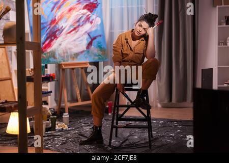 exhausted artist sitting on chair in painting studio and holding hands ...