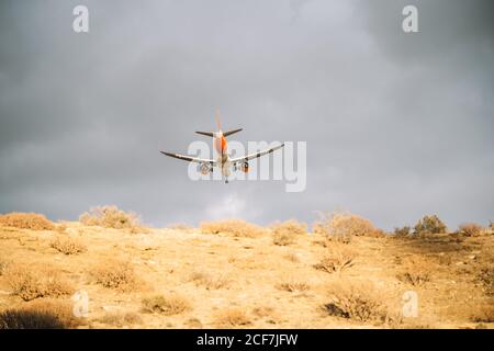 From below of white and orange aircraft flying with cloudy grey sky on background Stock Photo