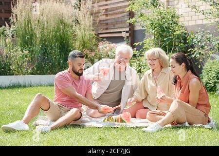 Family shot of senior man and woman having picnic with their young adult children on lawn Stock Photo