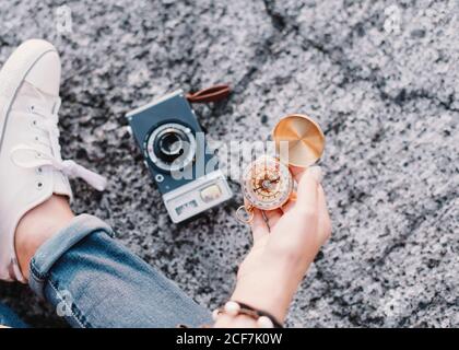 Crop female traveler sitting next to vintage analog photo camera and holding in hand antique golden compass Stock Photo