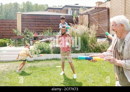 Children and adults spending great time in backyard shooting water guns, copy space Stock Photo