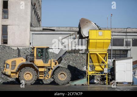 Bucharest, Romania - September 1, 2020: Earth mover operator arranging a pile of empty bottles in a glass recycling facility. Stock Photo
