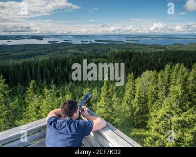 Back view of young man taking photos of beautiful landscape on digital camera in Finland Stock Photo