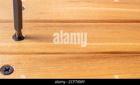 The screwdriver twists the self-cut into wooden boards. Construction tools, home repairs. Stock Photo