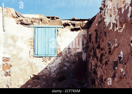 Window shuttered by blue wooden shutters in clay old wall of shabby ancient building in Fuerteventura, Las Palmas, Spain Stock Photo