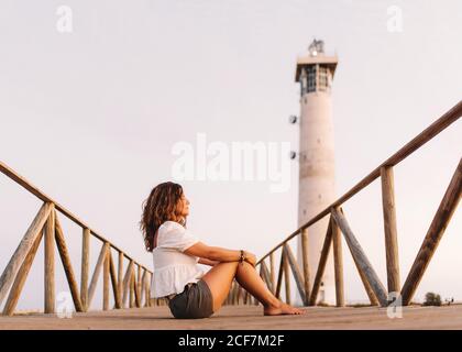 Woman sitting on bridge to lighthouse and looking away Stock Photo