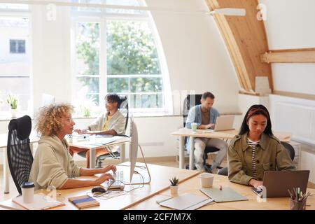 Group of business people in casual clothing sitting at their workplaces and using computers in their work at office Stock Photo