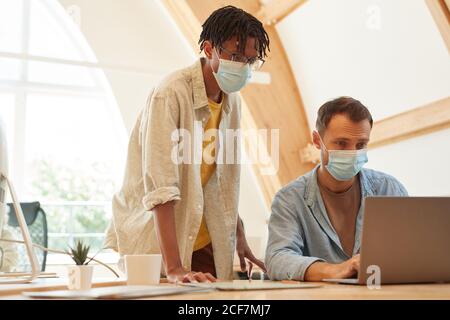 Software developers in protective masks using laptop in work they developing new program Stock Photo